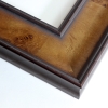 This large elegant frame is smooth and glossy due to its traditional veneer finish. The shine accentuates the honey brown tones that pop against the natural wood grain. The inner and outer lip of the profile is accentuated due to its dark contrast, as well as emphasized by the gradient featured within the scooped profile